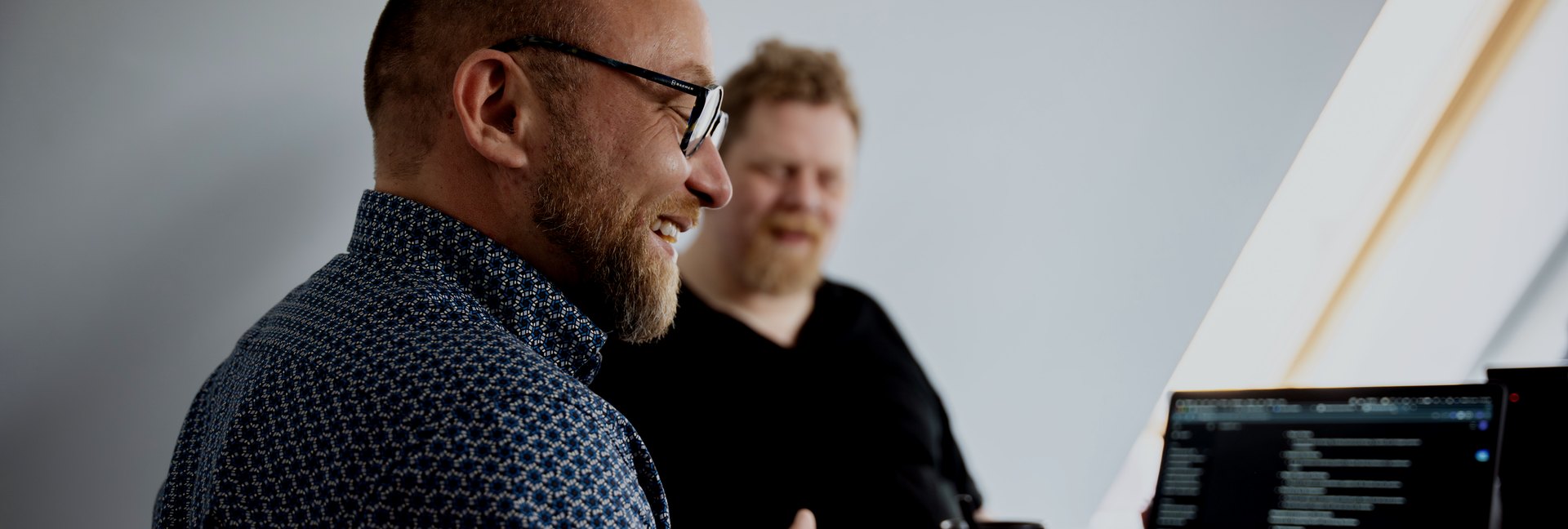 To kolleger i en uformel snak ved bordet, kode på skærmen ved siden af dem.
